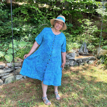 A woman in blue dress and hat standing on grass.