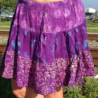 A woman wearing purple and blue skirt standing on grass.