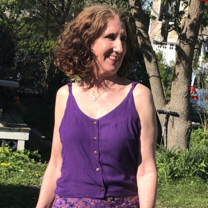 A woman in purple shirt and skirt standing next to tree.