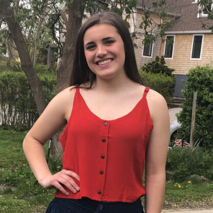A woman in red shirt standing next to trees.